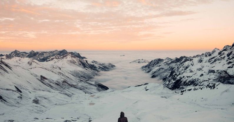 Elevation Gain - Person Standing in Snowy Field Under White and Orange Skies