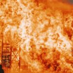 Fire Building - Silhouette of faceless people standing next to bright orange burning construction against dark sky in evening
