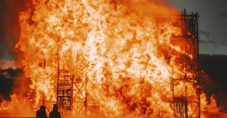 Fire Building - Silhouette of faceless people standing next to bright orange burning construction against dark sky in evening