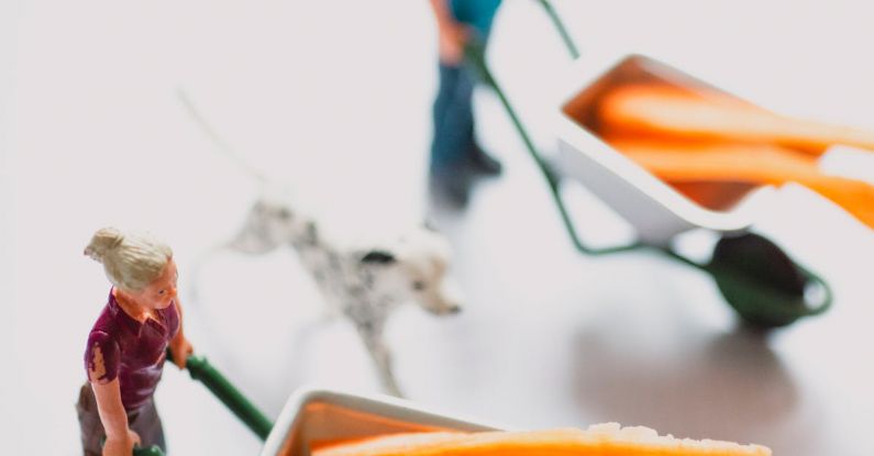 Small Acts - High angle of toys for children in shape of man and woman in uniform carrying wheelbarrow with orange sticks